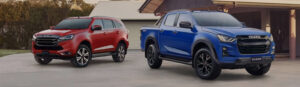 Two Isuzu vehicles—a red SUV and a blue pickup—are parked in a driveway in front of a house.